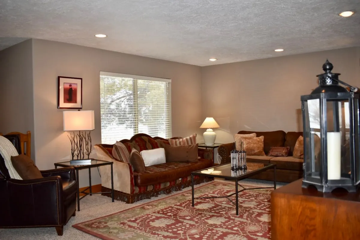 A cozy living room scene with a sofa adorned with pillows, a rustic coffee table, a stylish lamp, and a soft area rug. The inviting setup suggests a perfect spot for relaxing, reading, or sharing stories, with natural light enhancing the warmth of the space.