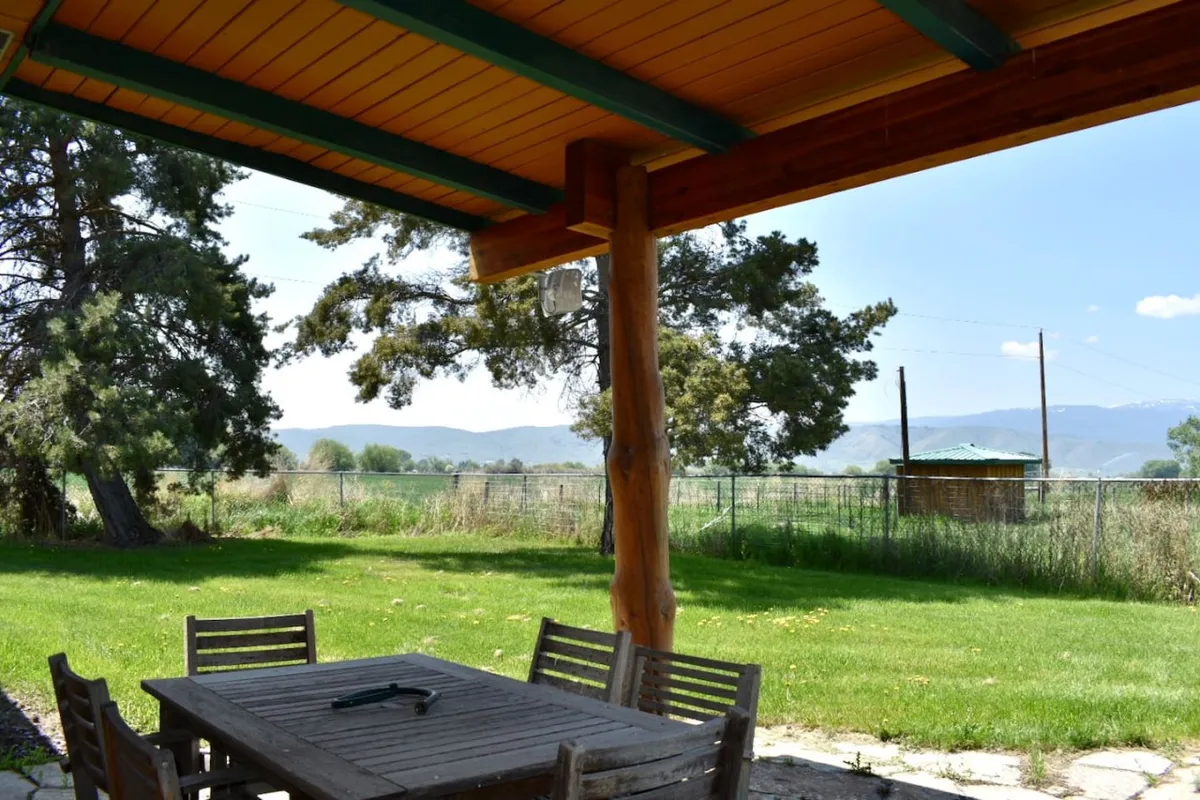 A serene exterior scene featuring a wooden table set in a grove of trees, with breathtaking mountain views unfolding in the background. The table is perfectly positioned for outdoor dining or relaxing, capturing the tranquil natural setting and the ranch’s connection to the surrounding landscape.