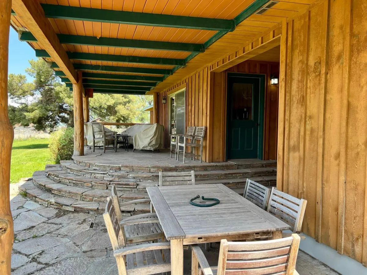 An outdoor wooden table and chairs sit atop stone steps, surrounded by greenery and a welcoming doorway. The layout invites guests to enjoy al fresco meals, evening conversations, or quiet mornings in the fresh air.