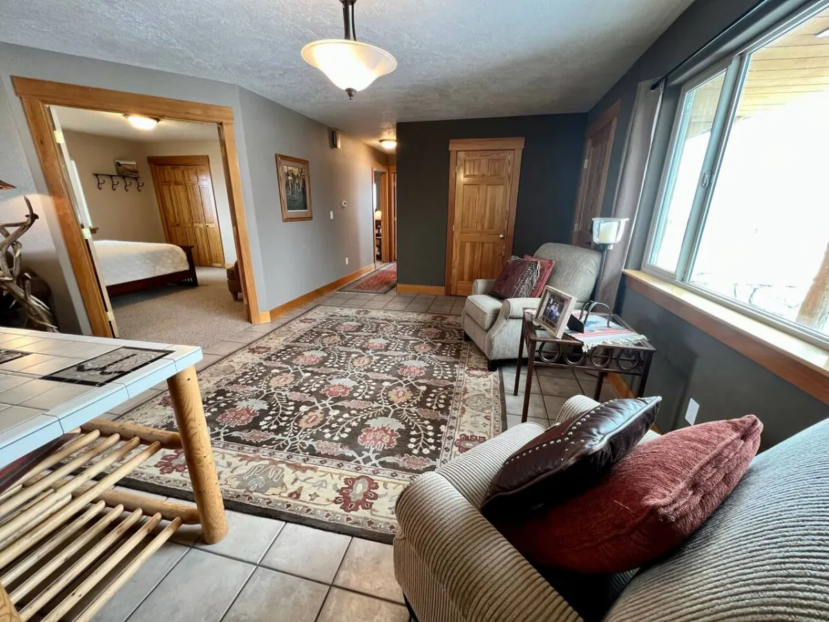 A comfortable and inviting living area featuring a cushioned sofa, decorative rug, large window letting in natural light, and a soft light fixture overhead. The setup is ideal for socializing, reading, or simply soaking in the peaceful ranch setting described in the section.