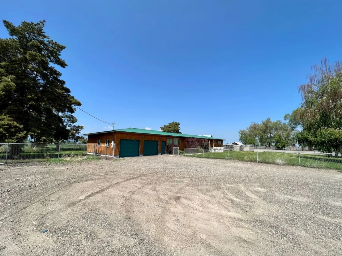 A rustic wooden structure with a green roof, set beside a gravel driveway and open outdoor areas. The scene feels accessible, inviting, and clearly connected to nature, hinting at the convenience of arrivals and departures as well as areas for pet care and outdoor enjoyment.