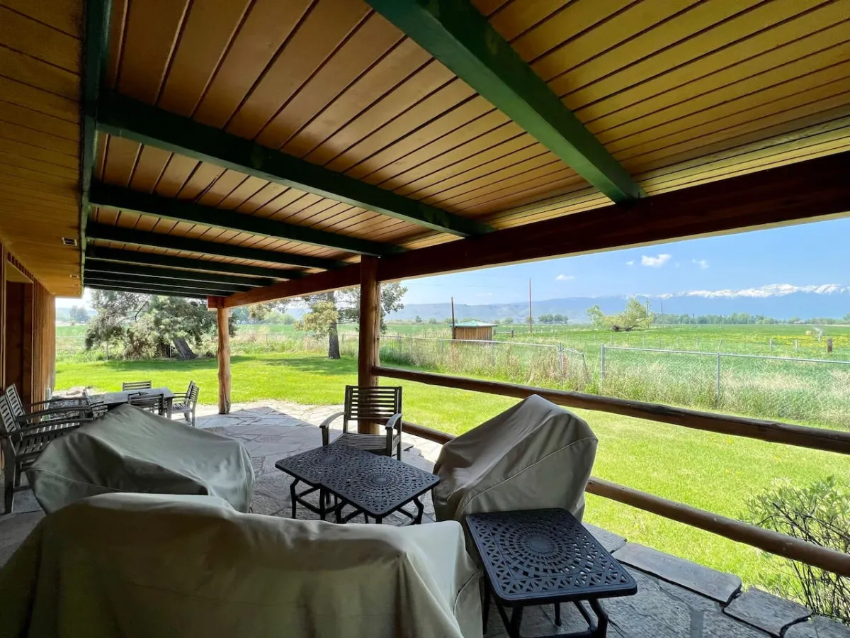 The exterior shot highlights a covered patio with outdoor furniture, green lawn, and a stunning mountain view in the distance. It's an inviting outdoor living space that encourages relaxing, entertaining, and soaking in the scenery.