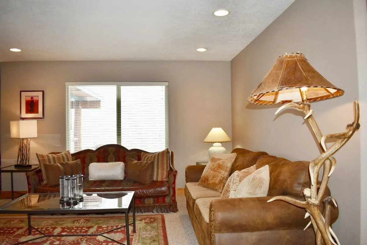 A spacious living room featuring a leather sofa, decorative lamp, coffee table, and artwork on the wall. The setting exudes warmth and comfort, with inviting seating areas ideal for family relaxation, conversation, or entertainment. The overall ambiance is cozy and perfect for movie nights or casual gatherings.