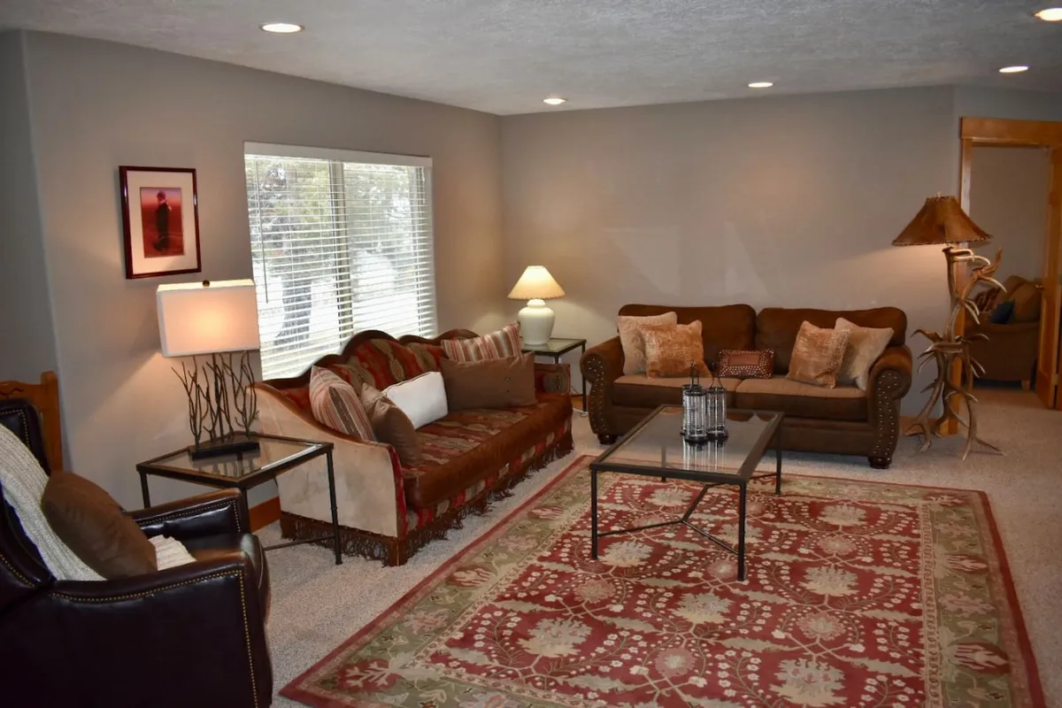 A sunlit living space featuring a cozy sofa with decorative pillows, a coffee table adorned with a lantern, and a large window that allows natural light to cascade into the room. The placement near the window suggests an opportunity to enjoy sweeping views from indoors.
